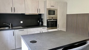 A modern kitchen with light wood cabinets, a black countertop, stainless steel appliances, and a built-in bench with storage. - Vacation home at Vogelsang (Meschede)