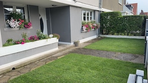 En boligejendom med en velholdt forhave, en stensti og blomkasser med pink og hvide blomster.