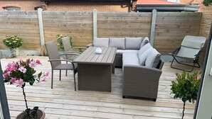 En terrasse med fletningsmøbler, heriblandt en sofa og stole, et bord og en lille potteplante.