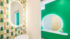 A bathroom with a white sink, a mirror with a circular frame, and a green wall with a geometric pattern.