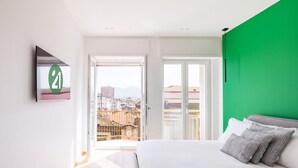 A bedroom with a bed, a green wall, a city view, and a door leading to a balcony.