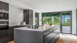A modern kitchen with a large island, dark cabinetry, and a view of greenery through a glass door. - "Heidie" - 600m from the sea by Interhome (Sjølund)