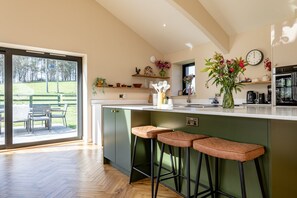 Una cocina moderna con una isla grande, taburetes de bar y vista a un espacio verde.