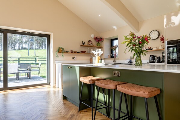 A modern kitchen with a large island, bar stools, and a view of a grassy area.
