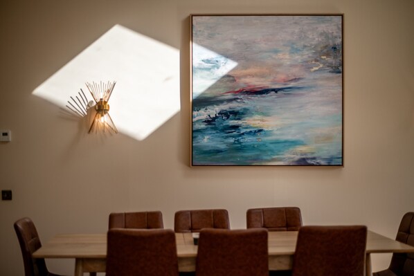 Un espace repas comprenant une table et des chaises, un tableau abstrait accroché au mur et un luminaire original.