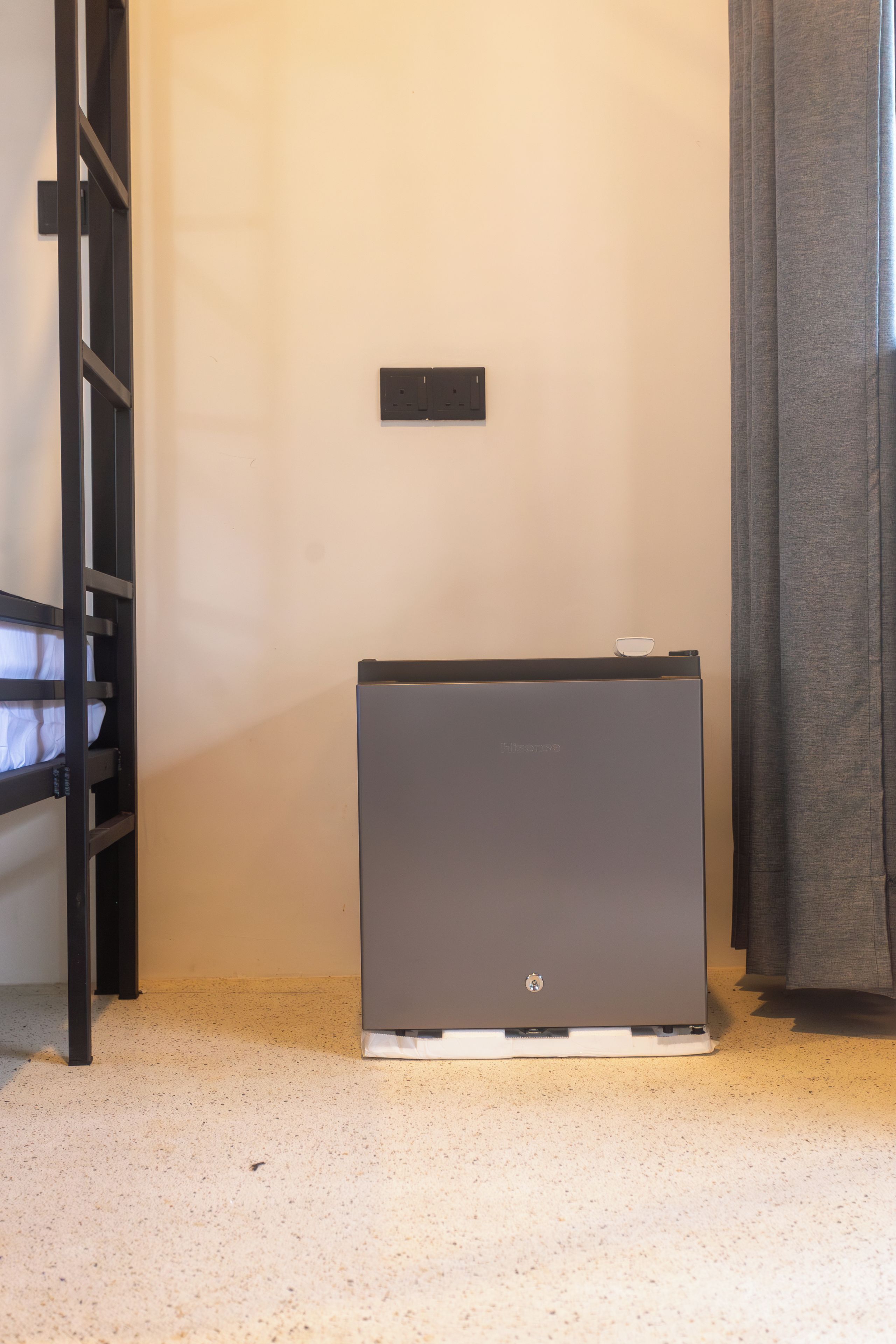 A compact room with a bunk bed, a small desk, and a compact refrigerator.