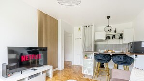 A modern living room with a flat-screen TV, a dining area with two chairs, a kitchen with a microwave, and a bar area. - Sweet cocoon at Disney (Montévrain)