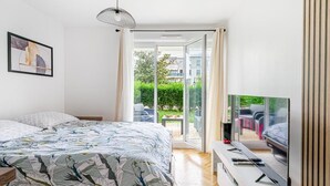 A bedroom with a bed, a TV, and a sliding glass door to a balcony. - Sweet cocoon at Disney (Montévrain)