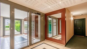 A hotel lobby with a glass door entrance, a green door, and a tiled floor. - Sweet cocoon at Disney (Montévrain)