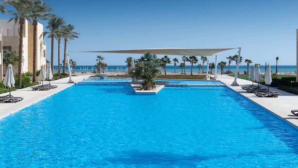A swimming pool with a view of the beach, surrounded by palm trees and sun loungers. - Xuru Stays I Homestyle 3BR Penthouse Pool & Beach View (El Gouna)