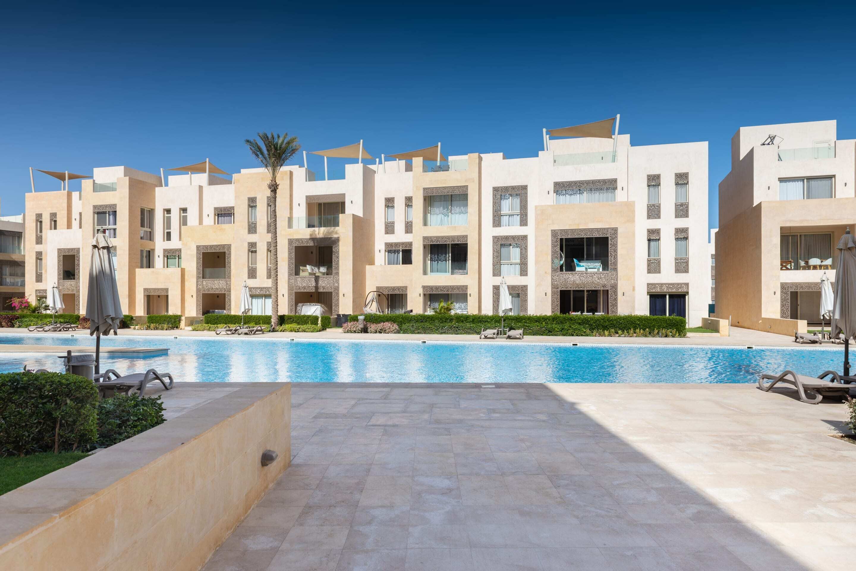 A modern hotel with a swimming pool, multiple balconies, and a well-maintained garden area.
