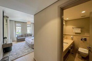 A modern hotel room with a bed, a sofa, a bathroom with a sink and toilet, and a view of the outside through a window. - Xuru Stays I Homestyle & Summery 1bdr@ Mangroovy Free Beach Pool (El Gouna)