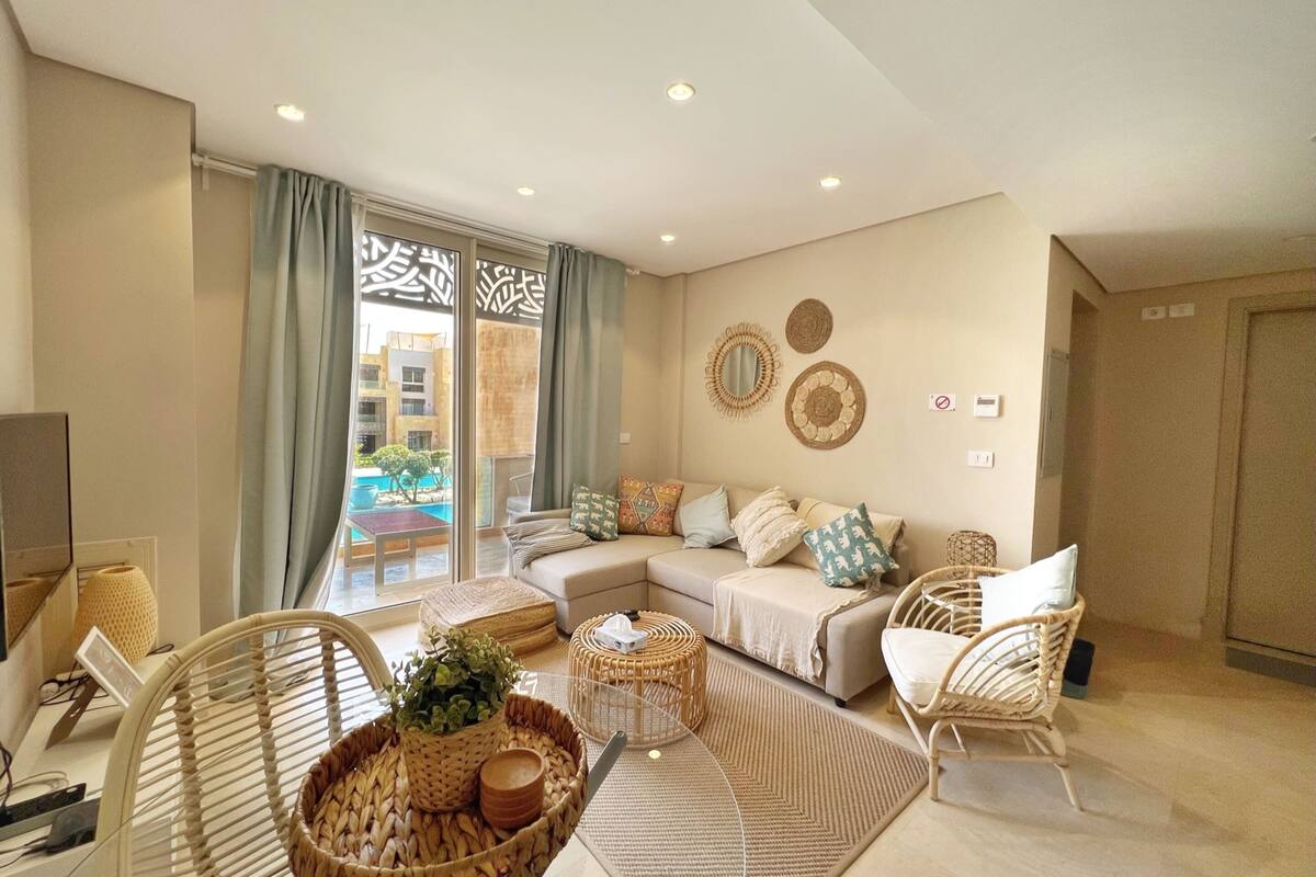 A modern living room with a sofa, wicker chairs, a coffee table, and a large window with curtains.