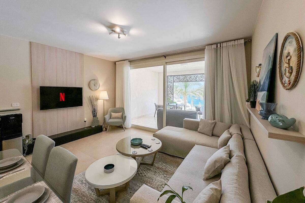 A modern living room with a flat-screen TV, a sofa, a coffee table, and a dining area.
