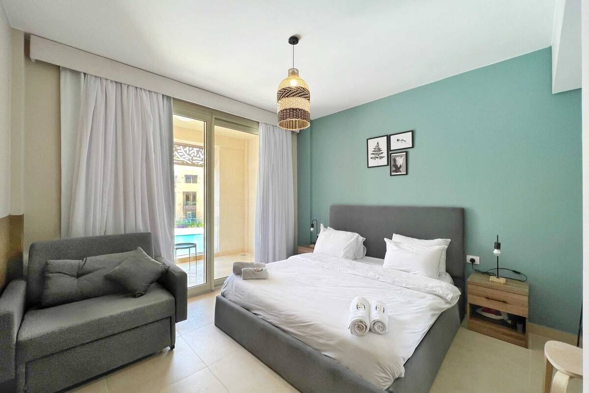 A bedroom with a bed, a sofa, a nightstand, and a hanging light fixture.
