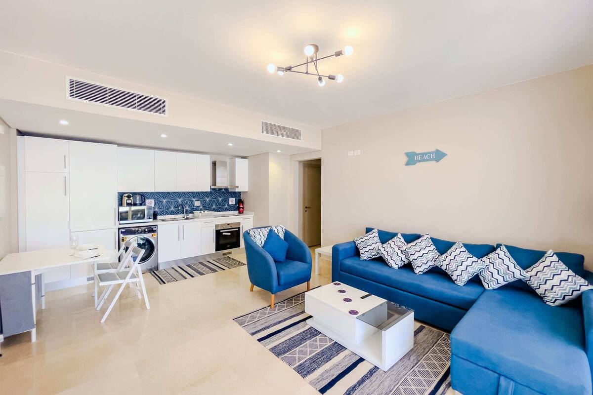 A modern living room with a blue sofa, a white coffee table, and a dining area with a white table and chairs.