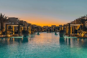 Ein Pool mit Sonnenuntergangsblick, umgeben von modernen Gebäuden und Palmen.