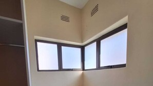 A kitchen with a white countertop, a window with a view, and a wooden stool.