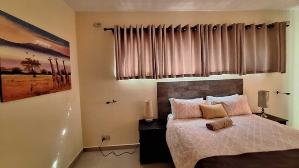 A bedroom with a bed, a nightstand, a painting, and a window with curtains.