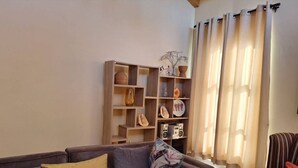 A living room with a sofa, a striped armchair, a wooden bookshelf, and a window with curtains.