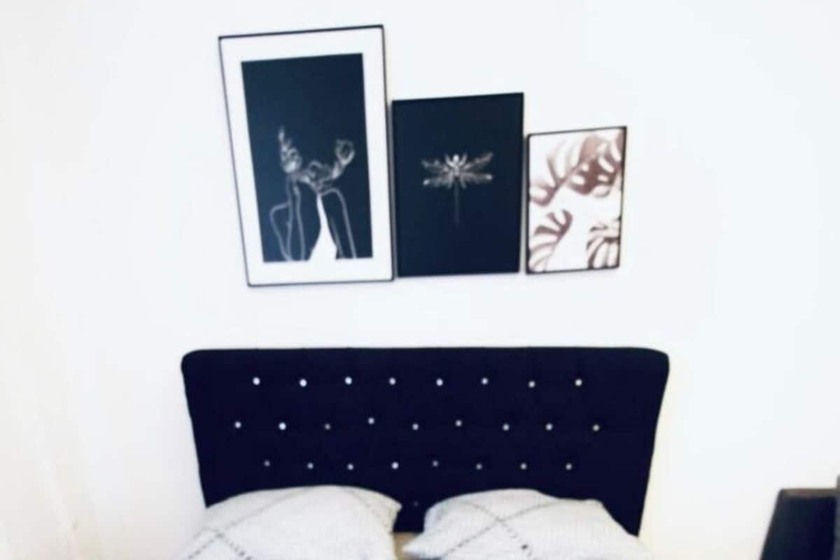 A double bed with a dark headboard and two pillows, a bedside table, and three framed pictures on the wall.