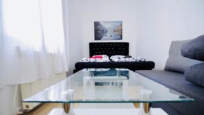 Ein modernes Wohnzimmer mit einem Glastisch, einem grauen Sofa und einem schwarzen Bettgestell mit einem dekorativen Kissen.