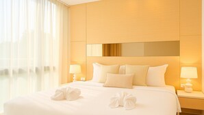 Ein Hotelzimmer mit einem großen Bett, zwei Nachttischen mit Lampen, einem großen Fenster mit durchsichtigen Vorhängen und einem Spiegel über dem Bett.