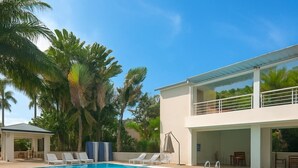 Ein Pool mit Liegestühlen, eine überdachte Sitzgelegenheit und ein zweistöckiges Gebäude mit Balkon.