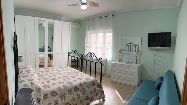 Un dormitorio con cama, cómoda, televisor, sofá azul y ventilador de techo.