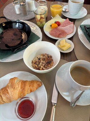 A breakfast table with various food items including a croissant, jam, coffee, and a bowl of cereal.