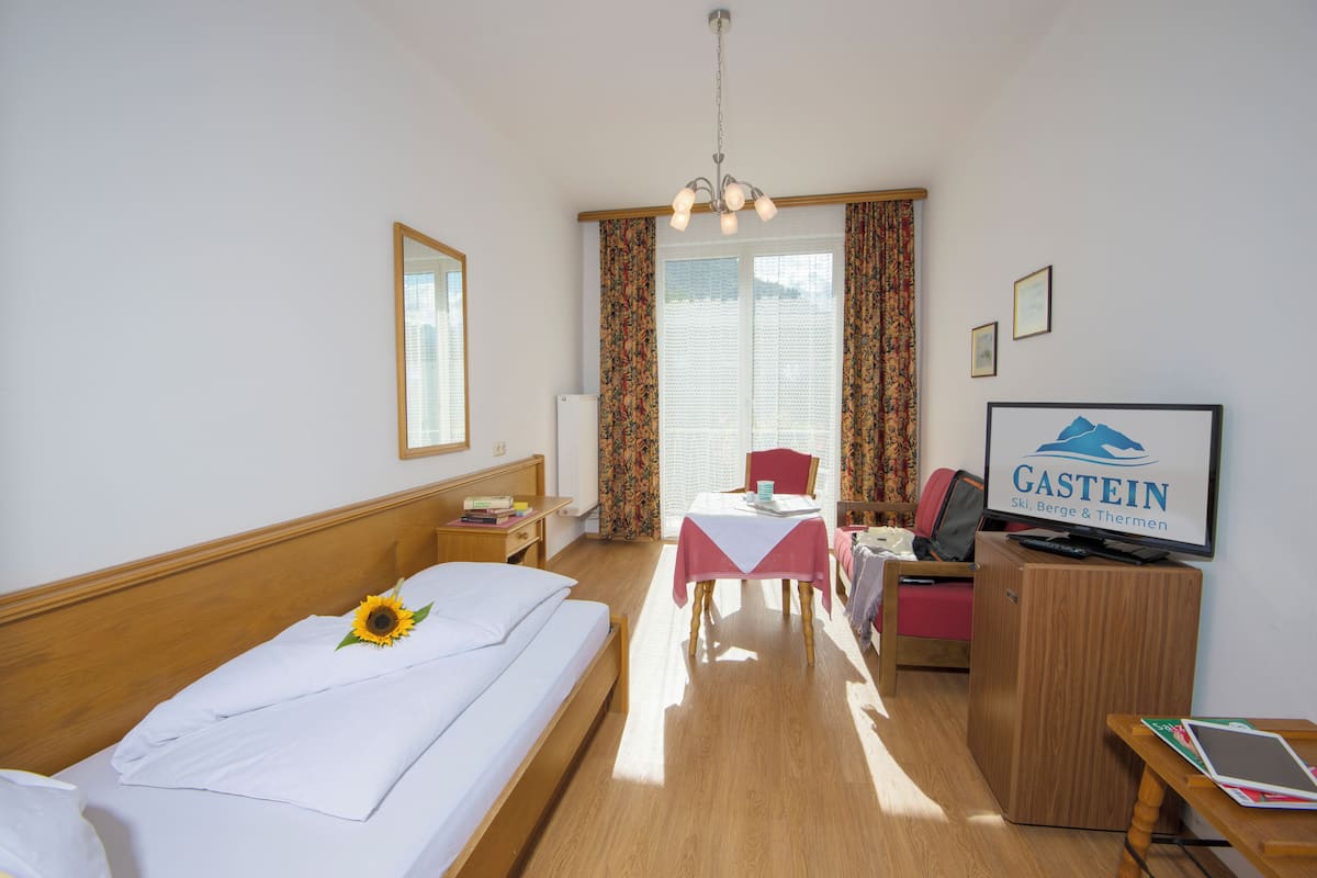 Hotellihuone, jossa on sänky, työpöytä, tuoli, televisio ja ikkuna, jossa on verhot.
