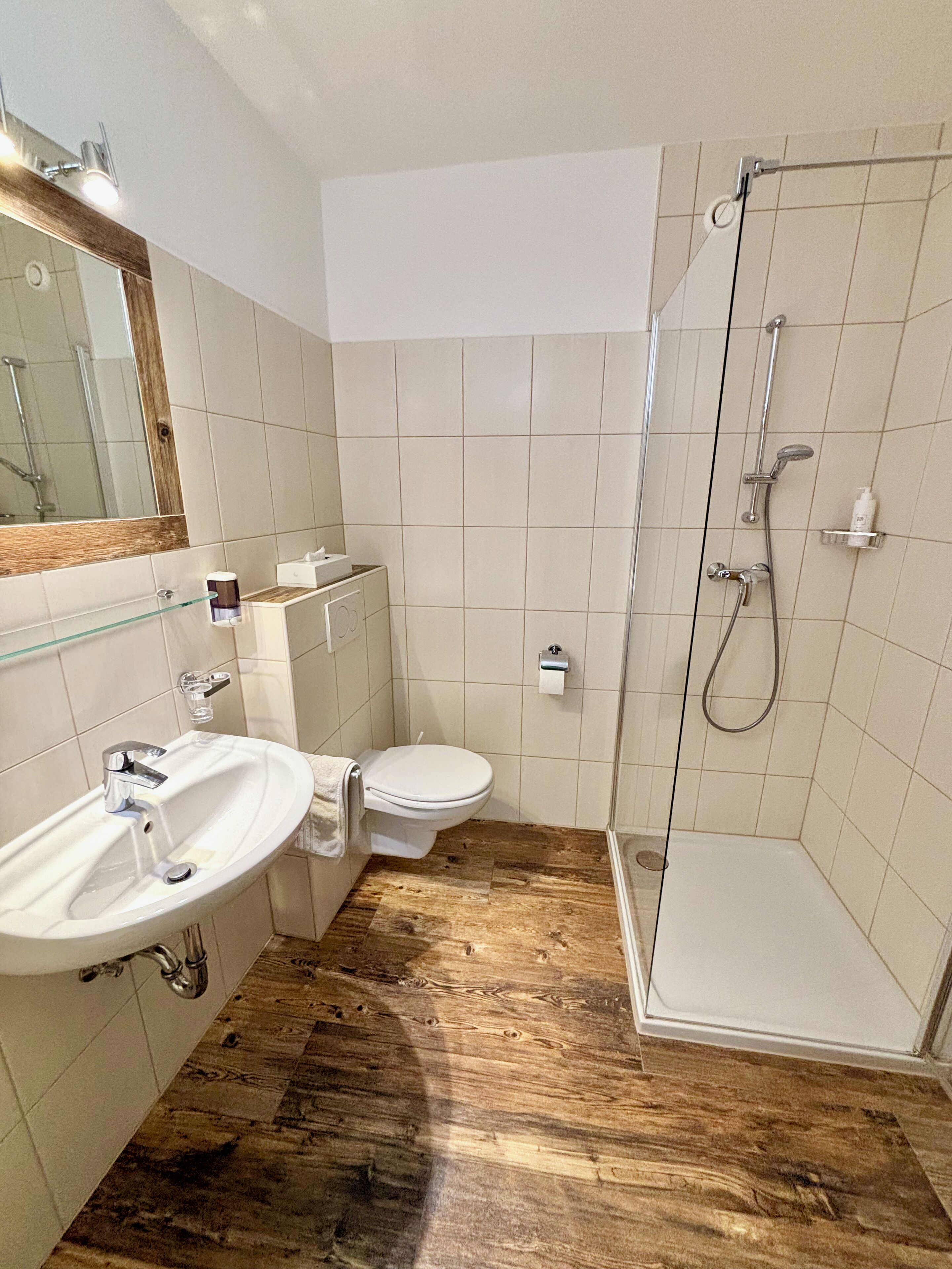 A bathroom with a wooden floor, a sink, a toilet, and a shower.