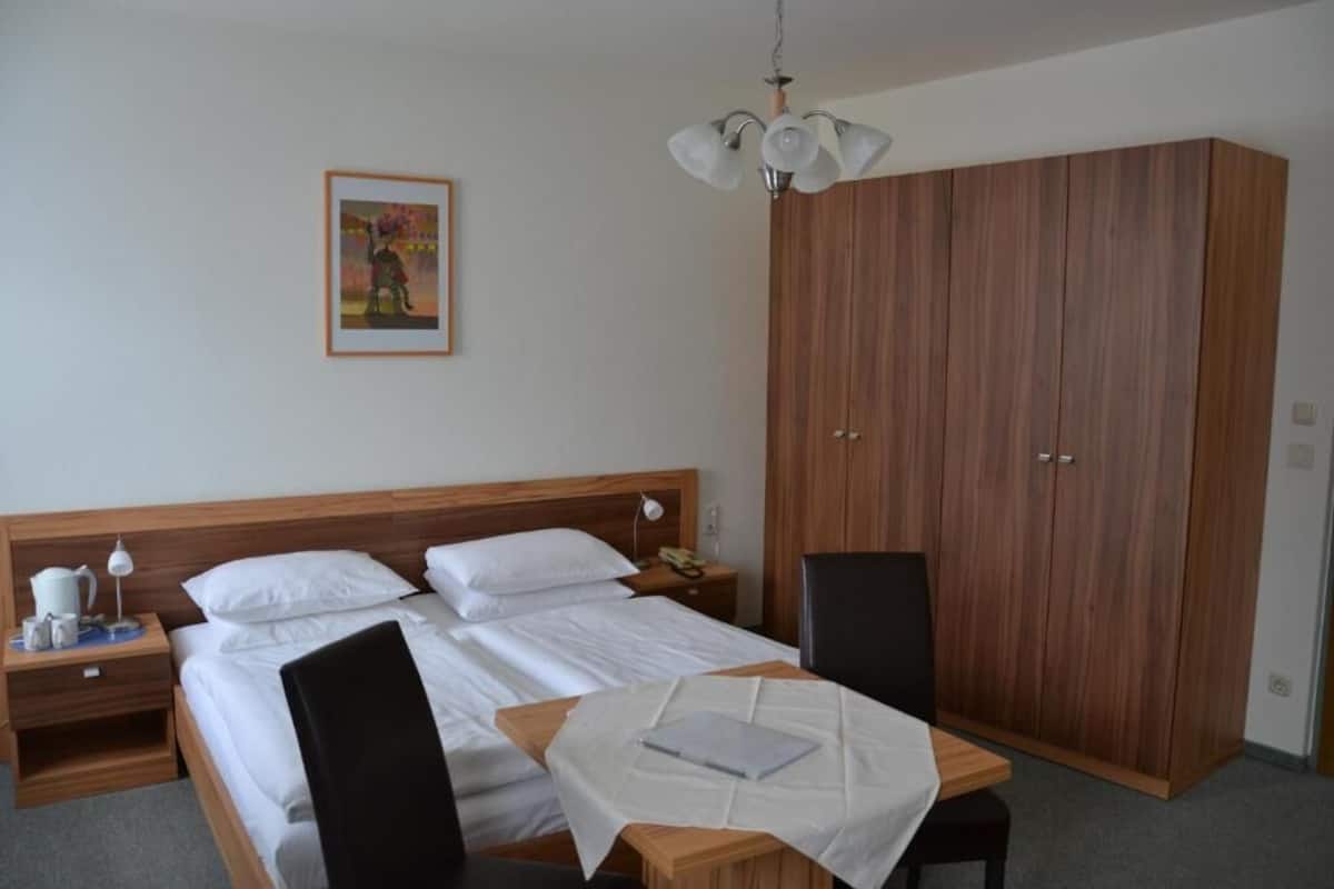 Hotellihuone, jossa on sänky, yöpöydät, työpöytä tuolilla, vaatekaappi ja kattovalaisin.