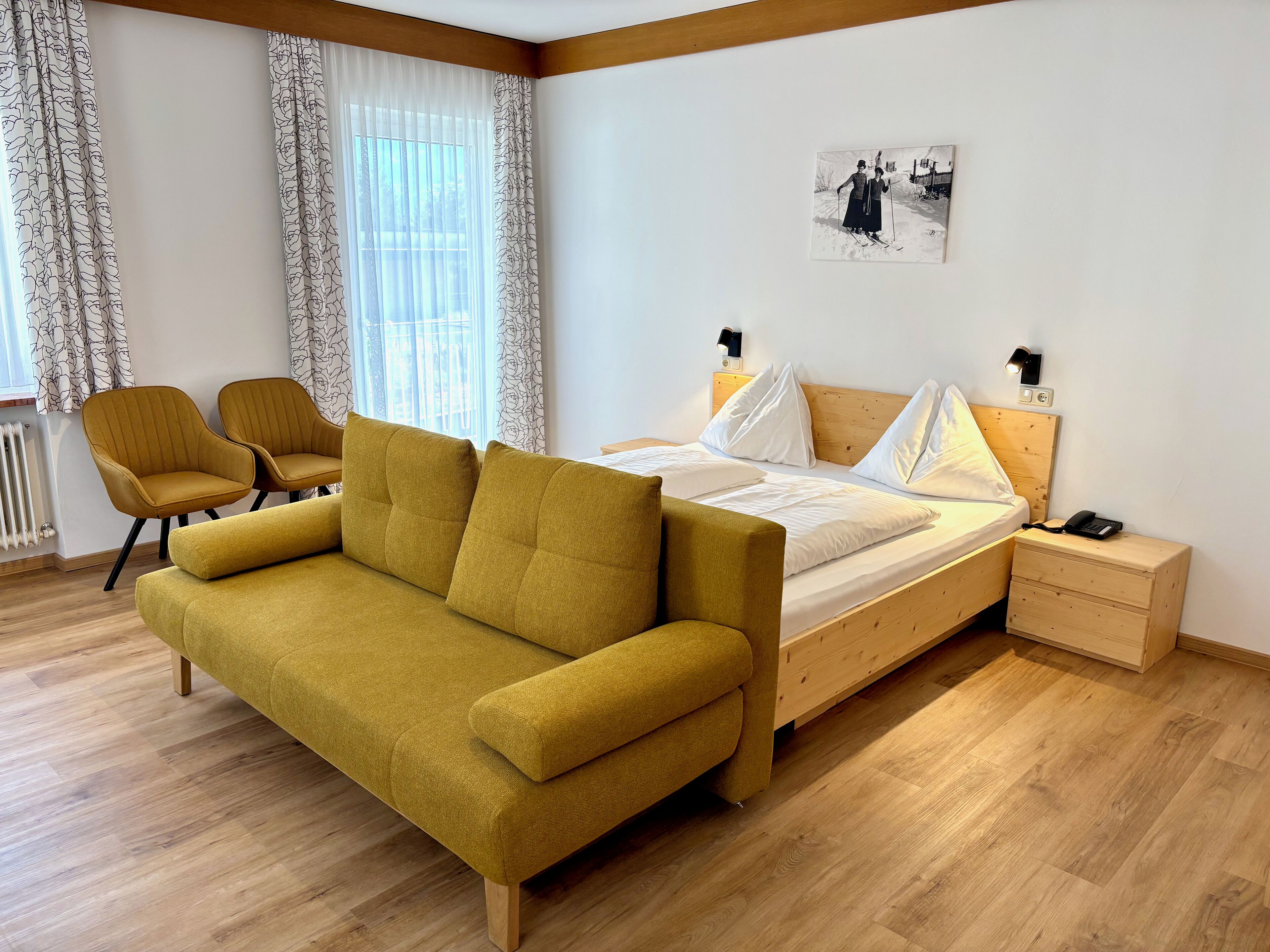 Ein modernes Schlafzimmer mit einem Bett, zwei gelben Sesseln, einem Holznachttisch und einem Fenster mit transparenten Vorhängen.