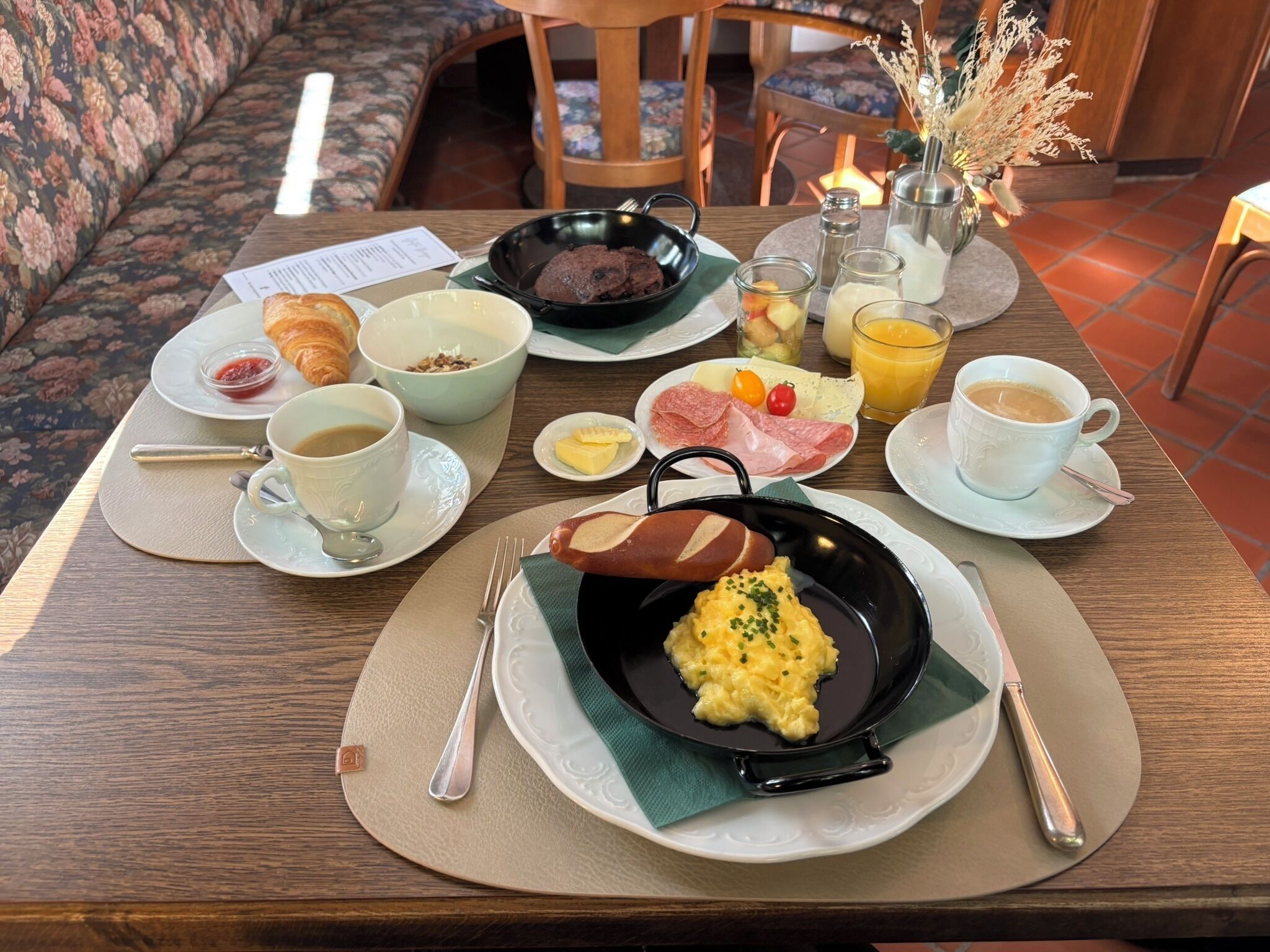 A breakfast setting with a variety of food items including eggs, croissants, and coffee on a wooden table.