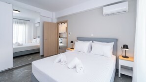 Et moderne hotelværelse med en stor seng, to sengeborde, et natbord, et spejl, en aircondition og udsigt til det tilstødende værelse.