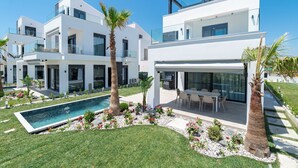 Et moderne hus med to etager, en swimmingpool, udendørs møbler og en velplejet have.