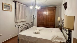 Una camera da letto con un letto, un lampadario, un armadio in legno, un comodino con una lampada e un quadro appeso al muro.