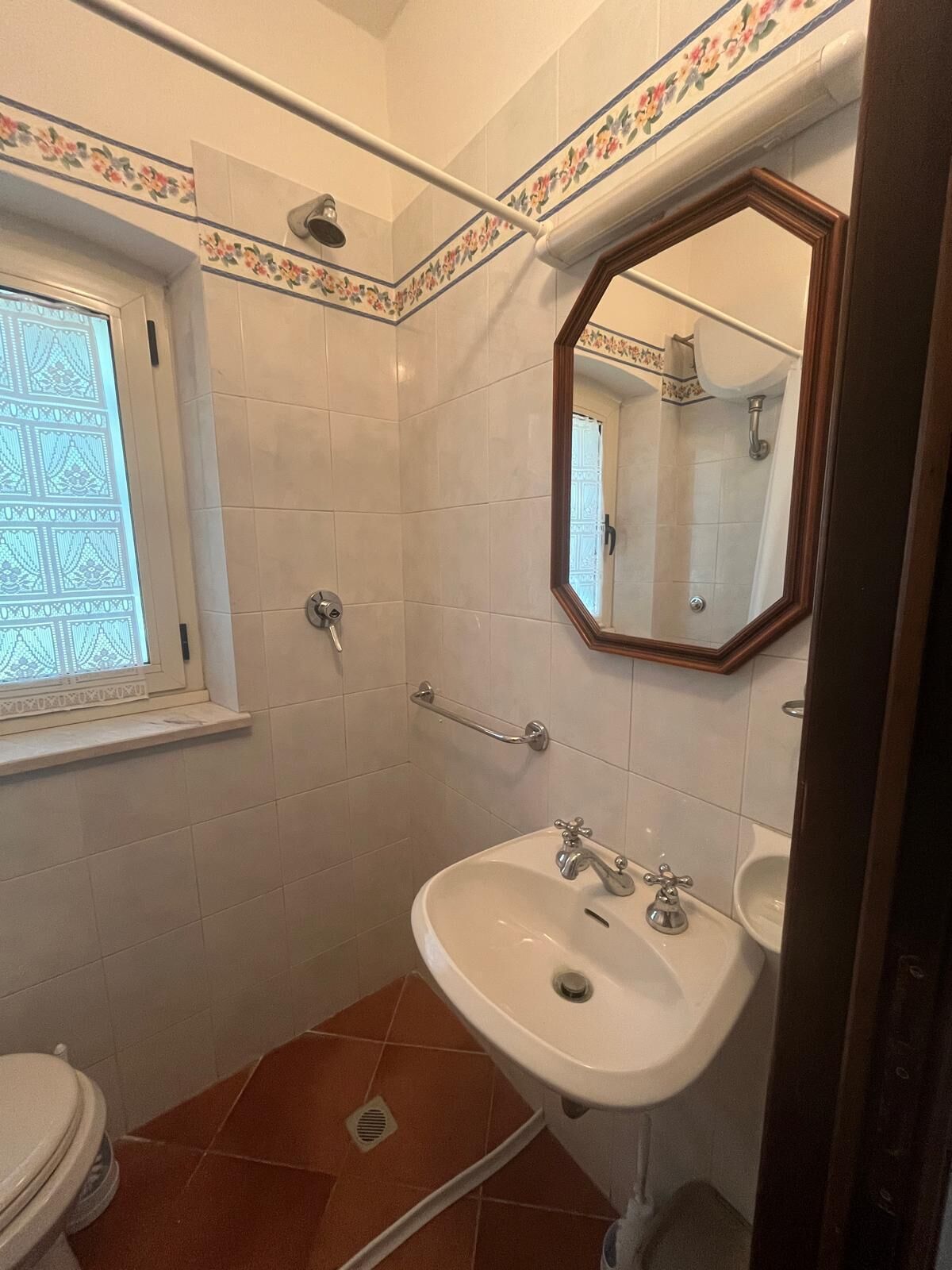 Un baño con inodoro, lavamanos, ducha y una ventana con azulejos decorativos.