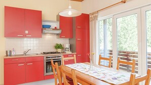 Eine moderne Küche mit roten Schränken, einem Holztisch mit roten Stühlen und einem großen Fenster mit Blick auf Bäume.