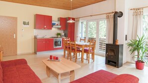 Ein gemütliches Wohnzimmer mit Holzbalkendecke, einem Essbereich mit Tisch und Stühlen, einer Küche mit roten Schränken und einem großen Fenster mit Vorhängen.