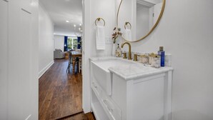 Une salle de bain moderne avec un meuble-lavabo blanc, des robinetteries dorées et un grand miroir avec éclairage intégré.