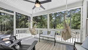 Une véranda couverte avec un ventilateur de plafond, des sièges d’extérieur et une vue sur la forêt environnante.
