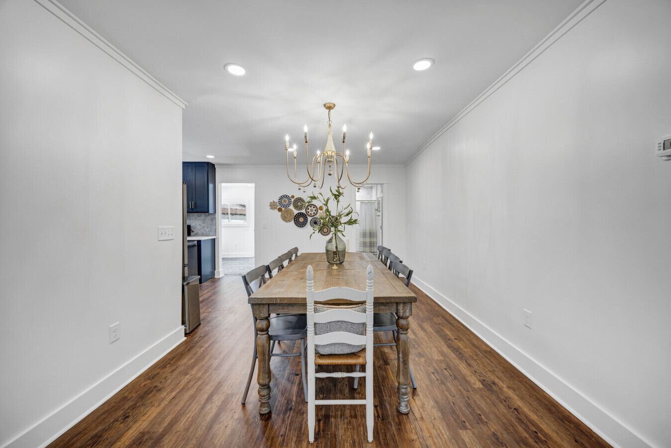 A dining room with a wooden table, white chairs, and a chandelier.