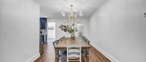 A dining room with a wooden table, white chairs, and a chandelier.