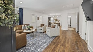 Un salon spacieux avec un canapé marron, des fauteuils à rayures et une table basse. Un tapis à motifs recouvre le plancher en bois.