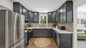 Une cuisine moderne avec des meubles de couleur sombre, des appareils en acier inoxydable, un tapis rond en fibres naturelles et une fenêtre laissant entrer la lumière naturelle.