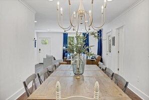 Un comedor con una mesa de madera, sillas, una araña y un florero con plantas.