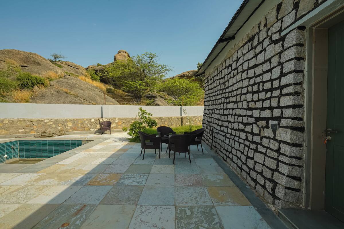 A patio with a pool, stone wall, and outdoor seating area.