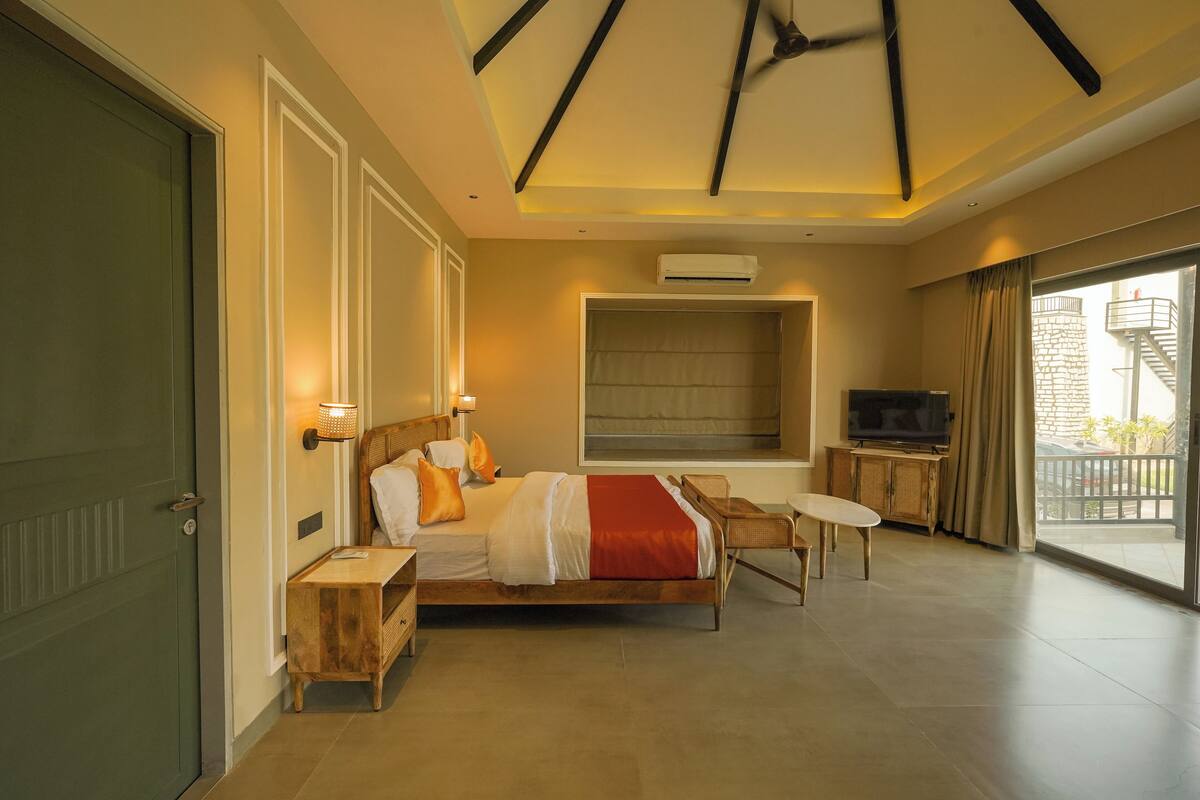 A hotel room with a bed, bedside table, TV, and a balcony with a view.